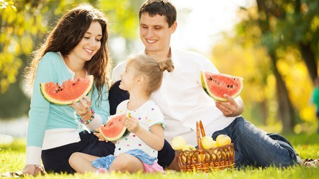 A small family enjoys eating watermelon in a park