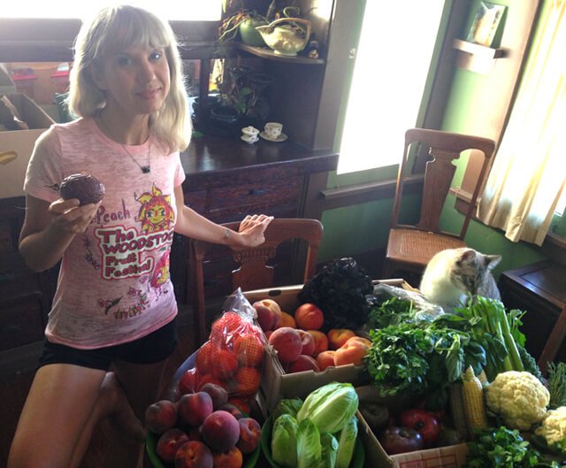 Anji Bee of Happy Healthy Vegan photographed with a large quantity of fruits and vegetables