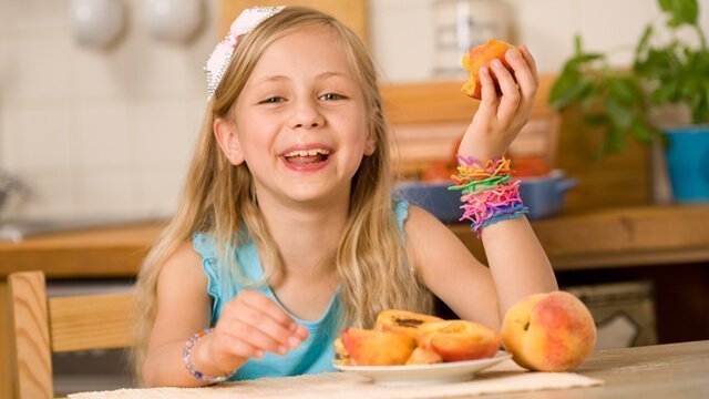 A girl eating peaches from a plate