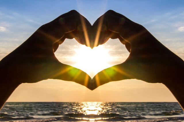 A man's hands cradle the sun in the shape of a heart