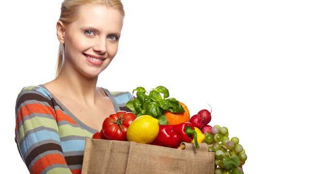 A woman holds a bag full of fruits and vegetables