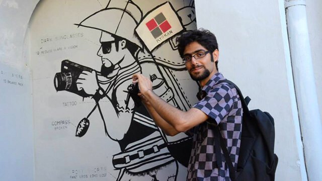 Moein Nejad holds a camera in front of a painting
