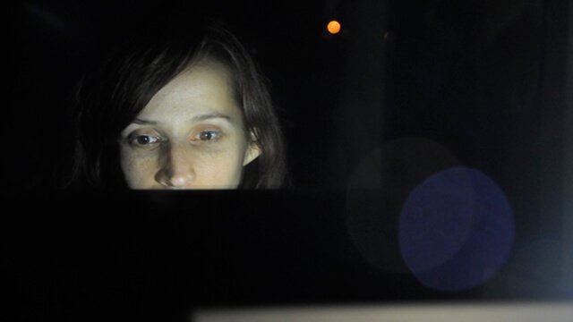 A woman reads from a computer screen in a dark room