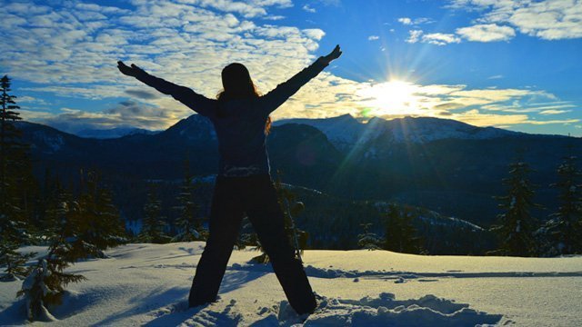 Tarah Millen facing the sun while standing in snow and with arms raised in a "V"