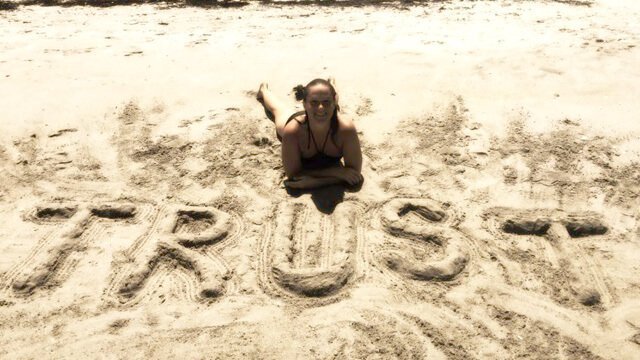 Tasha Lee sitting beside the word "Trust" written in sand